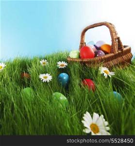 Basket of easter eggs on green grass and flowers