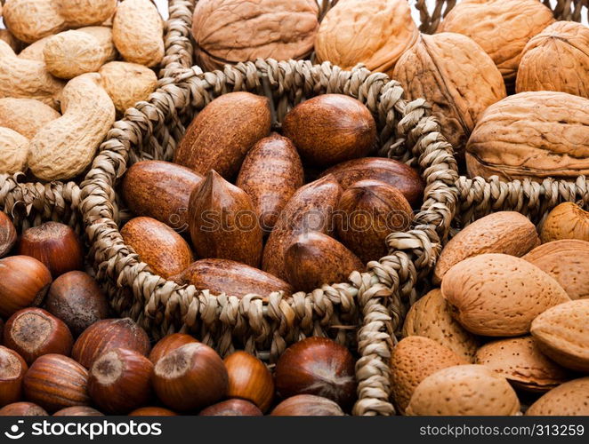 Basket reach in various kinds of nuts in shells, pecans, almonds, hazelnuts, peanuts and walnuts on white background