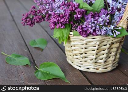 basket with branch of lilac on wooden background