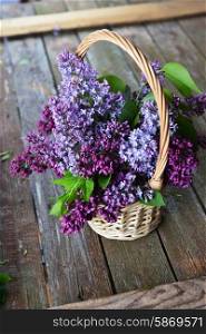 basket with branch of lilac on wooden background
