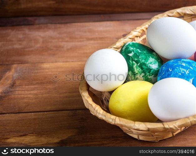 basket with colorful easter eggs and flower on wooden table