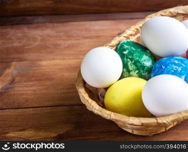 basket with colorful easter eggs and flower on wooden table