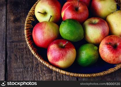 Basket with different fruits. Harvest ripe apples and lime in stylish dish on wooden background