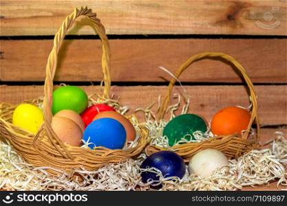 basket with Easter colored eggs and straw from the farm on rustic wooden background with space to write