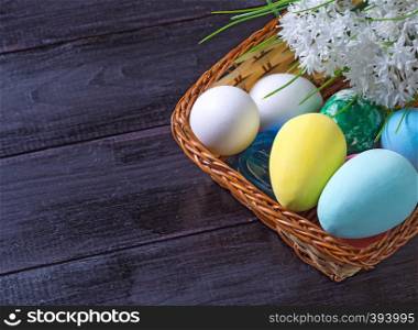 Basket with Easter eggs and bouquet of flowers on a dark wooden background
