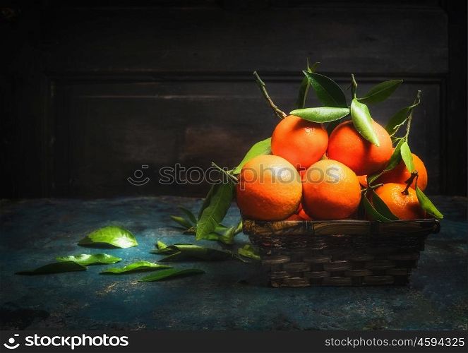 Basket with Fresh tangerines with green leaves on dark rustic background, side view