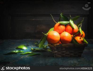 Basket with Fresh tangerines with green leaves on dark rustic background, side view