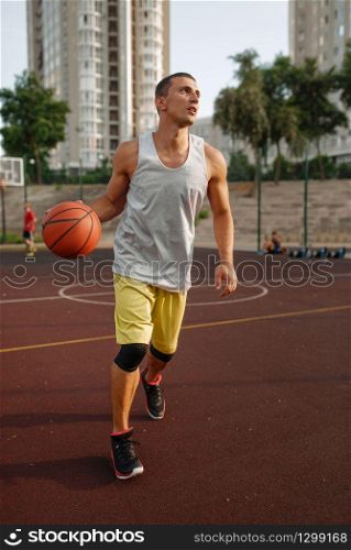 Basketball player goes on throw on outdoor court. Male athlete in sportswear holds ball on streetball training
