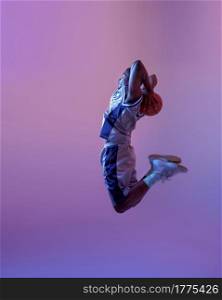 Basketball player jumping with ball in studio, neon background. Professional male baller in sportswear playing sport game. Basketball player jumping with ball in studio