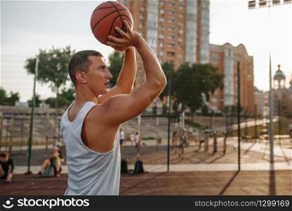 Basketball player makes a throw on outdoor court. Male athlete in sportswear shoots on streetball training, jump in action. Basketball player makes a throw on outdoor court