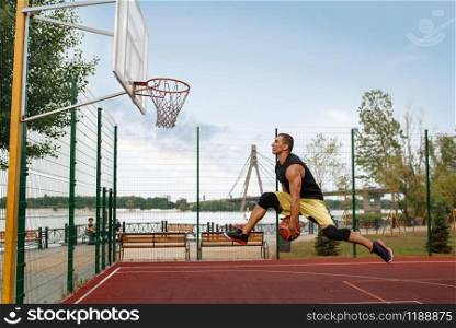 Basketball player makes a throw, shoot in jump, outdoor court. Male athlete in sportswear scores on streetball training. Basketball player makes a throw in jump, outdoor