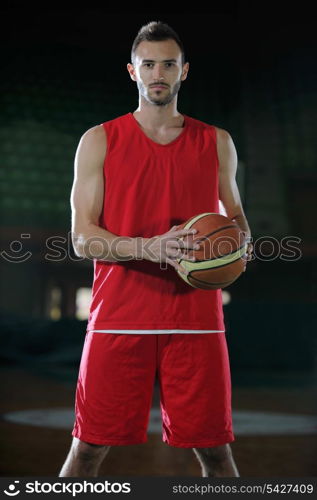 Basketball player portrait on basketball court holding ball with black isolated background