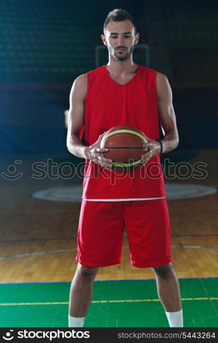 Basketball player portrait on basketball court holding ball with black isolated background