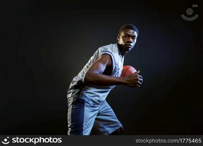 Basketball player, training with ball in studio, black background. Professional male baller in sportswear playing sport game, tall sportsman. Basketball player, training with ball in studio