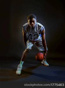 Basketball player with ball, practicing in action in studio, black background. Professional male baller in sportswear playing sport game, tall sportsman. Basketball player with ball, practicing in action