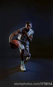 Basketball player with ball, practicing in action in studio, black background. Professional male baller in sportswear playing sport game, sportsman. Basketball player with ball, practicing in action