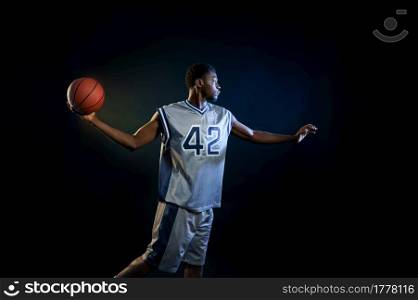 Basketball player with ball, practicing in action in studio, black background. Professional male baller in sportswear playing sport game.. Basketball player with ball, practicing in action