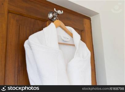 bath, clothes, hygiene and luxury concept - close up of two white bathrobes hanging on wooden hanger at home or hotel