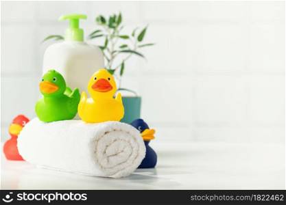 Bathroom accessories on white bathroom countertop against tile wall - white towel, rubber ducklings and house plant, copy space