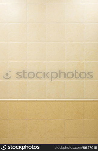 Bathroom wall, finished with square beige ceramic tiles with a marble pattern of light and dark shades. Architectural background