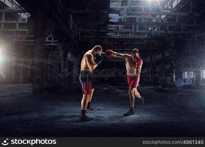 Battle of two boxers. Strong boxers fighting in dark industrial interior mixed media