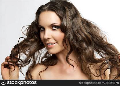 bautiful girl with brown, curly and long hair. She is turned of three quarters, playing with hair, looks in to the lens and smiles