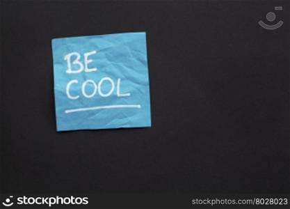 Be cool reminder - white marker handwriting on a sticky note against black paper background