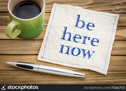 Be here now - motivational handwriting on a napkin with a cup of coffee