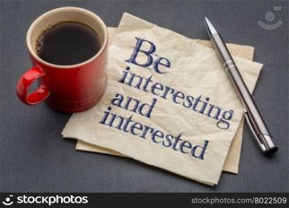 Be interesting and interested advice or reminder - handwriting on a napkin with cup of coffee against gray slate stone background