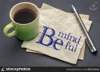 Be mindful - handwriting on a napkin with cup of coffee against gray slate stone background