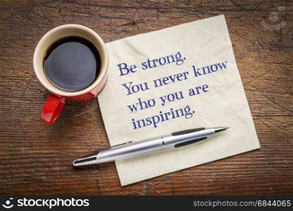 Be strong. You never know who you are inspiring.. Be strong. You never know who you are inspiring. Inspirational handwriting on a napkin with a cup of coffee.
