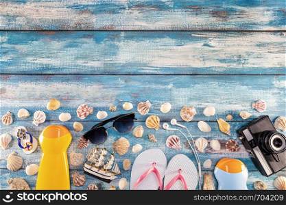 Beach accessories retro film camera sunglasses flip flop and sea shell on wooden. Top view of beach accessories on blue plank summer holiday banner travel concept. Focus on shells.