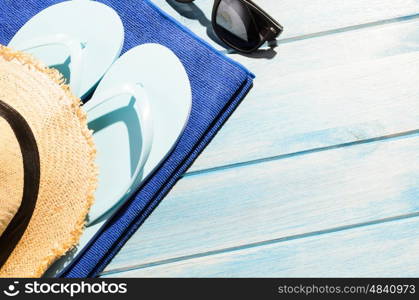 beach accessories. stylish sunglasses with flip flops, hat and towel on blue wooden table
