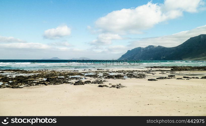 Beach and Mountains - beautiful coast in Caleta de Famara, Lanzarote Canary Islands. Beach in Caleta de Famara is very popular among surfers.. Beach and mountains - beautiful coast in Caleta de Famara, Lanzarote Canary Islands.