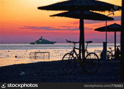 Beach and parasols on colorful sunset with large yacht view, Adriatic sea, Zadar, Dalmatia region of Croatia
