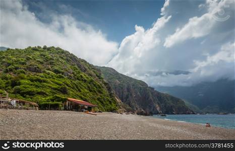Beach bar at Plage de Bussaglia with maquis covered rocks and clouds in background