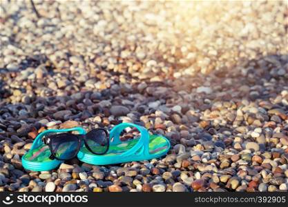 Beach blue sandals and sunglasses on the seashore stones. Vacation and travel concept. Beach blue sandals and sunglasses on the seashore stones