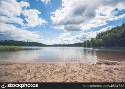 Beach by a beautiful forest lake with clouds in the sky