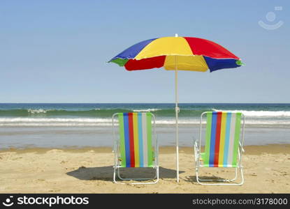 Beach chairs and umbrella on the ocean shore with surf in the background, horisontal