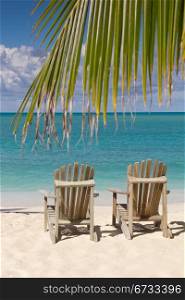 Beach chairs on white sand beach with cloudy blue sky and sun