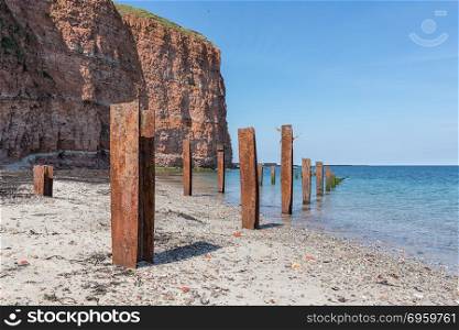 Beach Helgoland island with red cliffs and rusty iron pillars. Beach Helgoland island with red cliffs and rusty iron pillars of old putrefied jetty