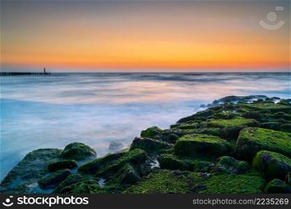 Beach in The Netherlands at the province Zeeland with windy sea weather and a long exposure image. Landscape showing sea waves and a breakwater at sunset