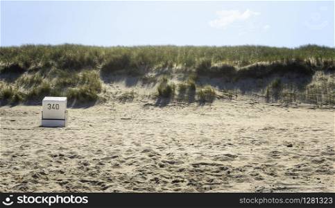 Beach landscape on Sylt island, with grassy dunes and single beach chair. Minimalist beach scenery.