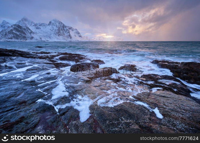 Beach of Norwegian sea on rocky coast in fjord on sunset in winter. Vareid beach, Lofoten islands, Norway. Coast of Norwegian sea on rocky coast in fjord on sunset