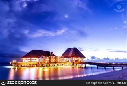 Beach restaurant glowing with bright lights in the night, romantic place for date on tropical island, summer holidays concept