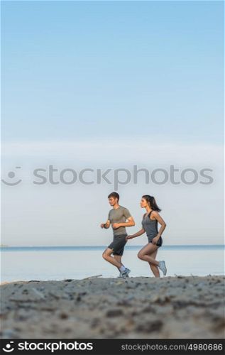 Beach running couple jogging outside. Runners training outdoors working out at seaside in the background. Fit multiracial fitness couple, Hispanic woman, Caucasian man.