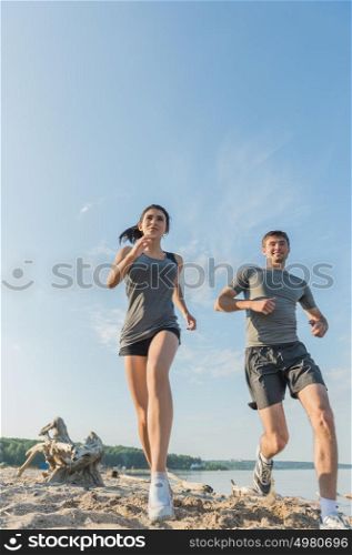 Beach running couple jogging outside. Runners training outdoors working out at seaside in the background. Fit multiracial fitness couple, Hispanic woman, Caucasian man.