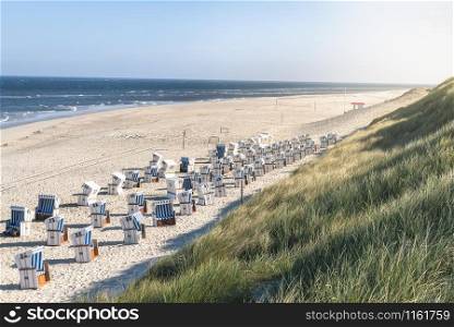 Beach scenery with sand, the North Sea water and marram grass dunes, beach chairs, on Sylt island, Germany. Wicker chairs and beach in summer heat.