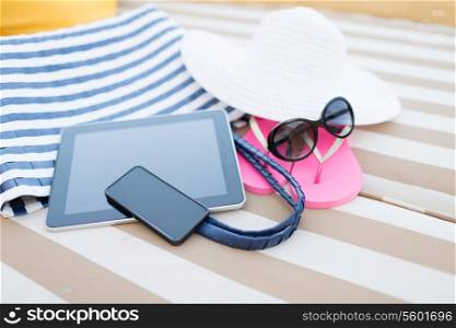 beach, summer, vacation, accessories and technology concept - close up of tablet pc computer, smartphone and summer accessories on beach