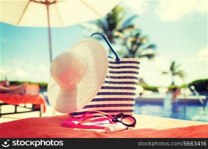 beach, summer vacation and accessories concept - close up of hat, bag, sunscreen and sunglasses at pool